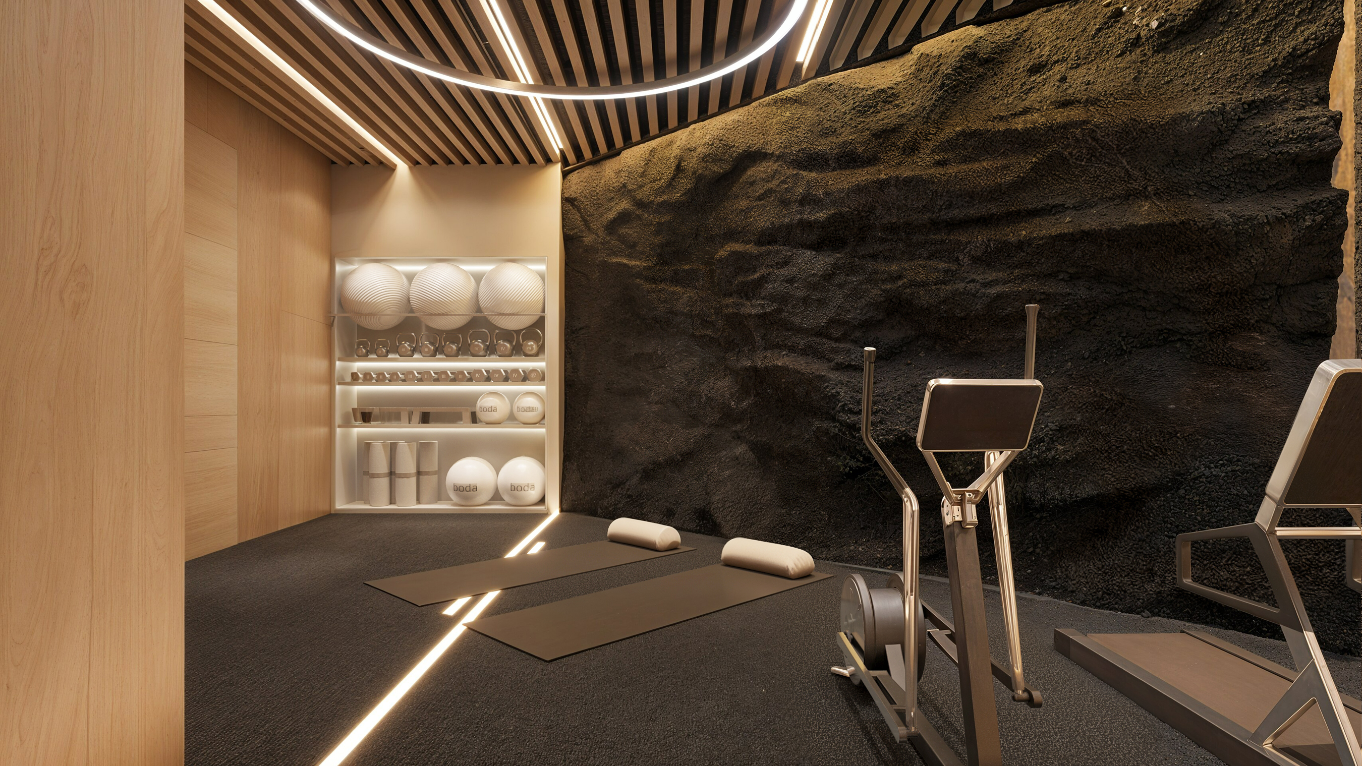 Detail view of the gym wall — mats laid on the floor, elliptical machine to the right, lava-rock backdrop