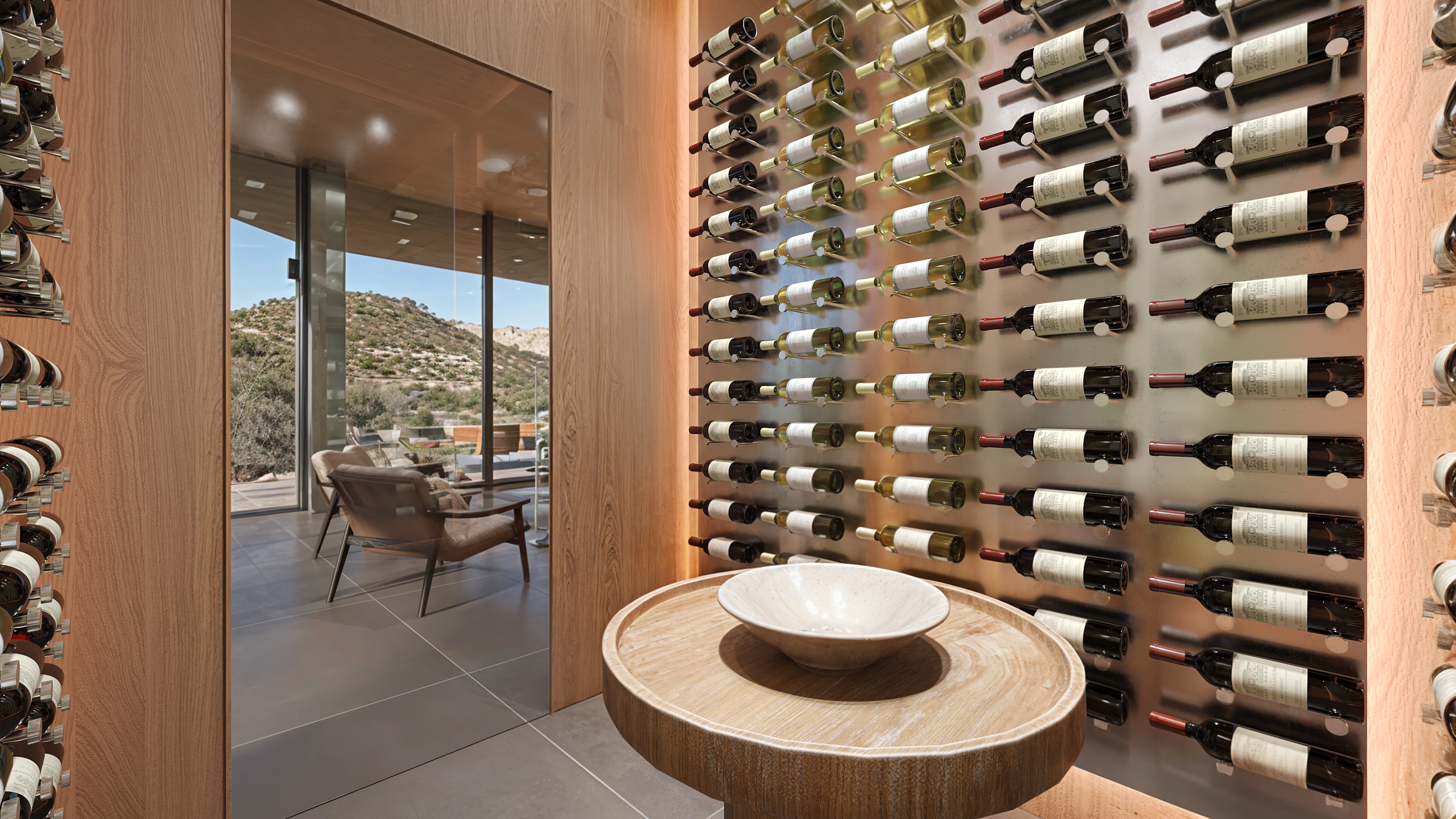Glass-walled wine cellar with steel bottle rails, a travertine tasting pedestal, and a glass door onto a terrace lounge with hillside views